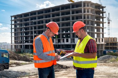 Üniformalı ve kasklı genç bir işçi, inşaat alanında çalışmak için üniformalı ve kasklı güçlü bir işçiden imza alıyor. İnşaat konsepti