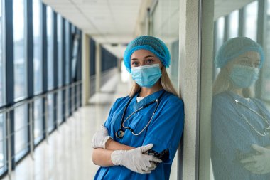 Koridorda maske takmış genç ve güzel bir hemşire duruyor.