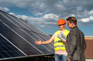 İki adam yeni güneş istasyonunun kurulum planını tartışıyor. Yeşil enerji kavramı, yenilenebilir enerji