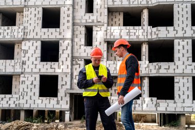 İşçiler işçi tulum ve kask giyip yeni binanın yanında duran bir planla güçlüler. İnşaat konsepti