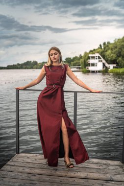 Gölde poz veren koyu kırmızı elbiseli güzel sarışın kız, romantik.