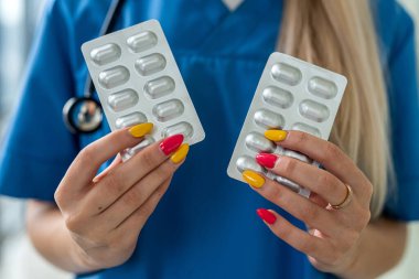 Eldiven giymiş genç bir hemşirenin ellerinde renkli haplar var.