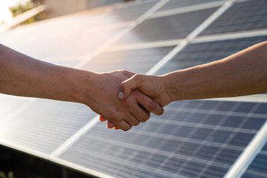Yenilenebilir enerji anlaşması tamamlandıktan sonra güneş paneline karşı el sıkışan iki kişi  