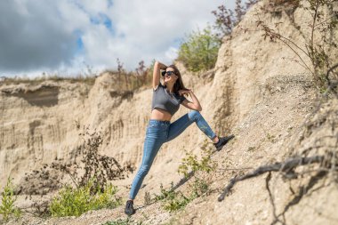 Taş ocağındaki kum kayalarının üzerinde poz veren sıradan giysili sıska bir kız. yaz zamanı