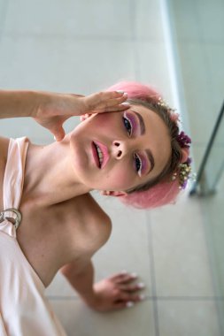 Bej elbiseli, profesyonel makyajlı ve kameraya poz veren genç ve güzel bir bayan.