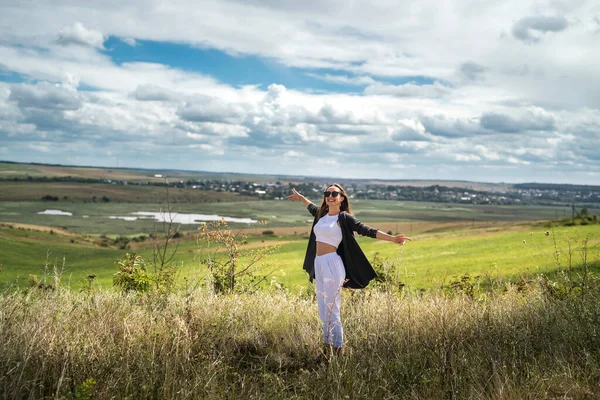 Çekici genç bir kadın yaz mevsiminde çimenlikte dikilirken eğleniyor. özgürlük