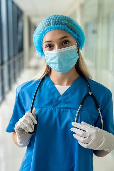 Genç hemşire koridorda duruyor ve elinde bir steteskop tutuyor.
