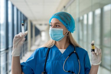 Koridorda elinde şırınga tutan üniformalı ve maskeli genç hemşire. Tıp konsepti