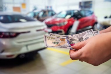 Manikürlü bir kadının genç ve güzel elleri, salonda arabalı yeni dolarların banknotlarını tutar. Araba alıp satma konsepti. İş konsepti