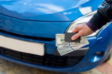 Erkek, mavi güzel bir arabanın arka planında dolar ve araba anahtarı tutan takım elbiseli bir adam. İş konsepti. Araba satın alma konsepti. İş konsepti
