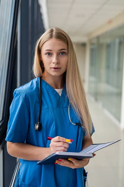 Piękna Blond Pielęgniarka Trzymająca Notatnik Długopisem Szpitalnym Korytarzu Koncepcja Medycyny — Zdjęcie stockowe