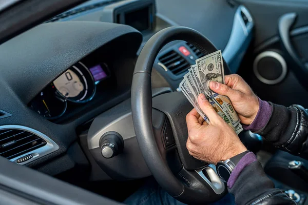 a strong bad criminal counts a large amount of dollar bills inside a car. The concept of robbery and crime
