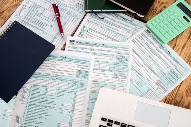 Vergi formları 1040 amerikan not defteri yeşil hesap makinesi kırmızı kalem ve dizüstü bilgisayar geniş bir masaya yayılmış. Belgelendirme kavramı