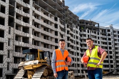 Üniformalı iki güçlü genç işçi yeni bir binanın arka planında duruyor. Yeni bir bina konsepti