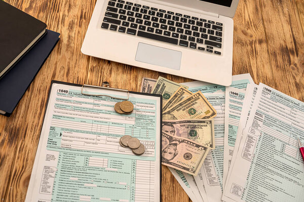 white notebook tax form usa 1040 with dollar bills and coins laid out on a wooden table. Business concept