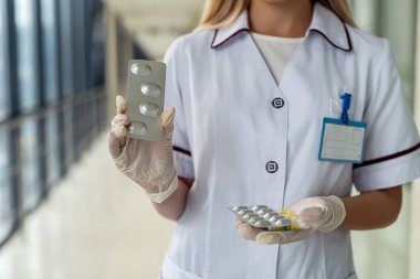 Eldiven giymiş genç bir hemşirenin ellerinde renkli haplar var.