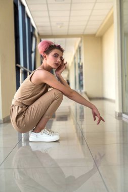 Koridorda yerde oturmuş kameraya poz veren genç bir kadın. 
