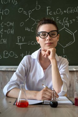 Kimya öğretmeni konik şişeyi renk sıvısı ile inceliyor. 