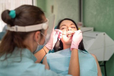 Dişçi sandalyesinde stomatolojik ayna olan hastanın dişine bakıyor.