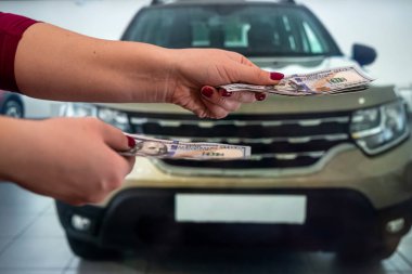 Manikürlü bir kadının genç ve güzel elleri, salonda arabalı yeni dolarların banknotlarını tutar. Araba alıp satma konsepti. İş konsepti