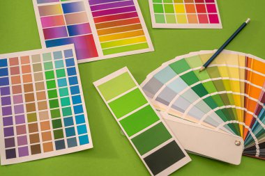 Renkli şablonlar kalem renklerinin kareleri yeşil bir arkaplanda yatar. Tasarım konsepti