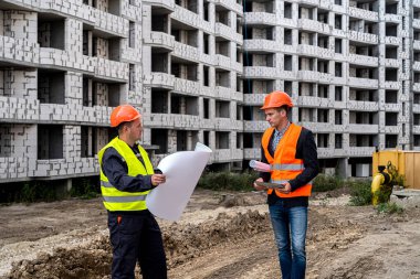 İşçiler işçi tulum ve kask giyip yeni binanın yanında duran bir planla güçlüler. İnşaat konsepti