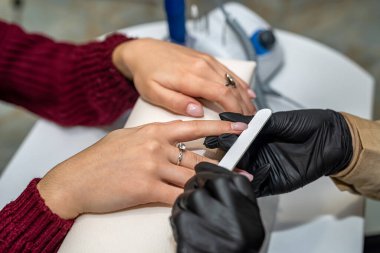 Özel eldivenli bir manikürcü salgın sırasında yeni bir müşterinin tırnaklarını testereyle kesiyor. Manikür konsepti. Kozmetoloji kavramı