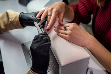 Özel eldivenli bir manikürcü salgın sırasında yeni bir müşterinin tırnaklarını testereyle kesiyor. Manikür konsepti. Kozmetoloji kavramı