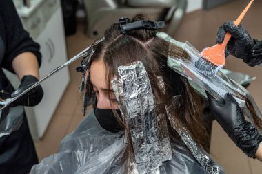 Koyu saçlı, güzel, genç bir kadın. Saçları açık renk, bukleler için özel bir araç. Seçkin bir salonda saç aydınlatma konsepti