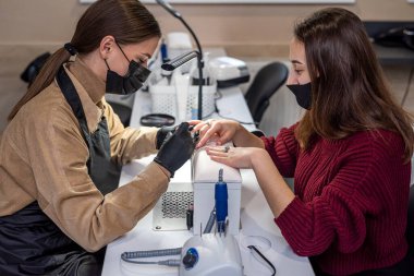 Çivi çakmada usta bir usta, kuaförde yeni bir müşteriye tırnak testeresi yapıyor. Salonda manikür konsepti