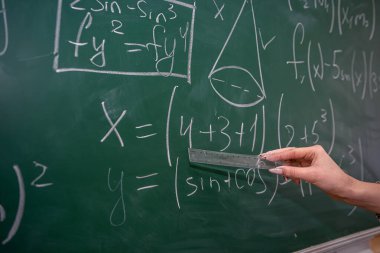 Tahtaya yakın güzel bir bayan öğretmen sınıfta, arka planda matematik öğreniyor.