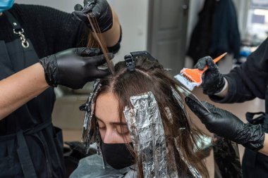 Bir salgın sırasında, kabinde maske takmış güzel siyah saçlı bir kız resmediliyor. Salonda salgın sırasında saç boyama konsepti