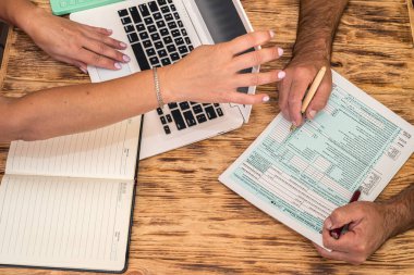 İşteki iki çalışan ofis masasında 1040 vergi formu dolduruyor. Vergi formu kavramı 1040