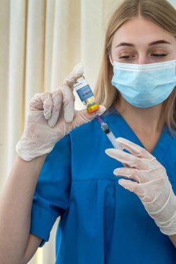 Maskeli ve eldivenli güzel sarışın hemşire bir hasta için aşı çeviriyor. Tıp konsepti