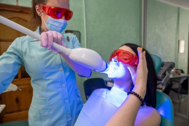 Ağzı açık bir hasta koruyucu gözlüklü bir dişçi koltuğunda oturuyor.