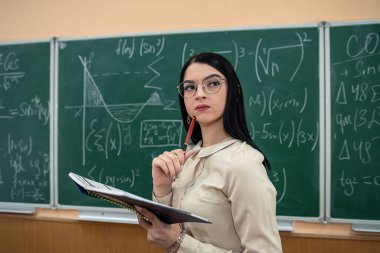 Sınıfta, tahtaya karşı matematik formüllü genç bayan öğretmenin portresi. eğitim kavramı