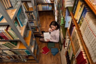 Güzel, sevimli, mutlu bir bayan modern bir kütüphanede birbiri ardına kitap okuyor. Kütüphane konsepti. Bilgi kavramı