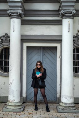 Siyah ceketli ve siyah ayakkabılı şık esmer yabancı bir şehirde sonbahar havası soluyor. Şehir konsepti. Sonbahar konsepti