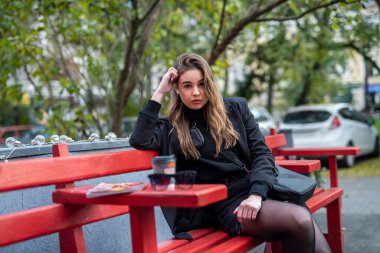 Siyah ceketli ve siyah ayakkabılı şık esmer yabancı bir şehirde sonbahar havası soluyor. Şehir konsepti. Sonbahar konsepti