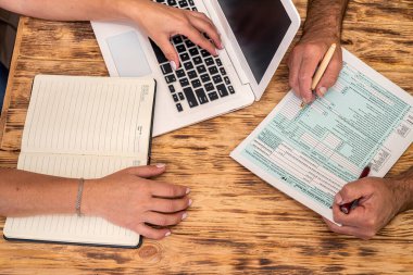 İşteki iki çalışan ofis masasında 1040 vergi formu dolduruyor. Vergi formu kavramı 1040