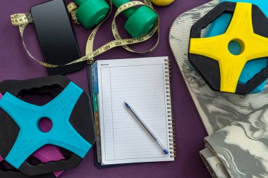 Bir defter ve kalemle birlikte yeni mükemmel ekipmanlar renkli paspaslara saçılmış. Spordaki gol kavramı. Sporda hedefleri olan not defteri konsepti