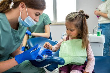Genç uzman dişçi kadın resepsiyona getirilen küçük bir çocuğun dişlerini fırçalıyor. Bebek dişlerini fırçalama konsepti