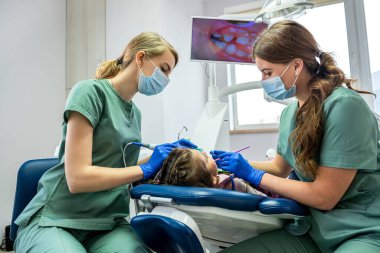 Küçük hasta, dişçiler tarafından ekranda gösterilen kamerayla muayene ediliyor. Çocukların dişlerini kamerayla incelemek.