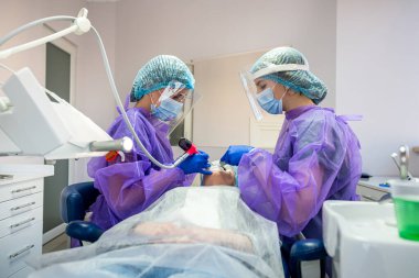 Diş hekimine eldiven ve maskeli özel giysiler içinde iki asistan hastanın sorunlu dişini ameliyat etmesi için dişçiye yardım ediyor. Diş hekimliğinde cerrahi kavramı
