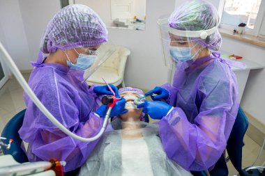 İç içe geçmiş diş sorunu olan bir hasta, bir dişçi ve asistanları tarafından ameliyat edildiği bir ameliyat sandalyesinde yatar. Dişçide ameliyat konsepti