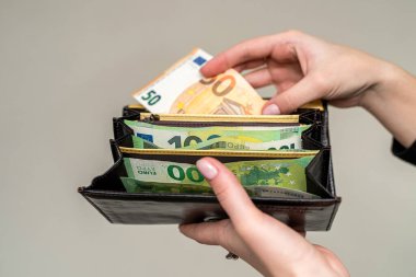 İçinde avronun bulunduğu cüzdanı tutan siyah takım elbiseli güzel, bakımlı genç eller. Cüzdandaki para kavramı