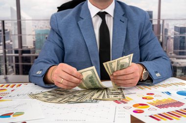 Şık genç iş adamı ofis masasında iş grafiklerini hesaplıyor. İş ve para kavramı