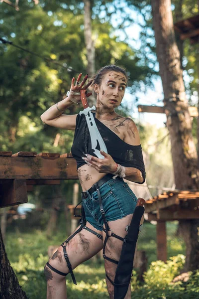 portrait of young woman wear short shorts with knife in forest.Woman smeared in the swamp holding a dagger posing in the woods