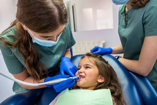 young qualified dentists in special clothes treat the teeth of a little girl in a dental chair. The concept of dentistry and children