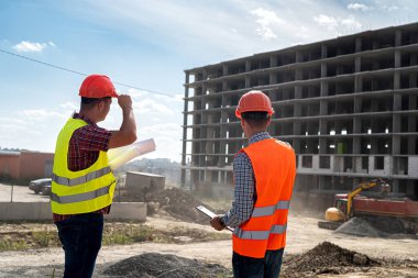 Özel giyimli ve üniformalı iki genç işçi inşaat alanında bir ev inşa etme sürecini tartışıyor. İnşaat konsepti